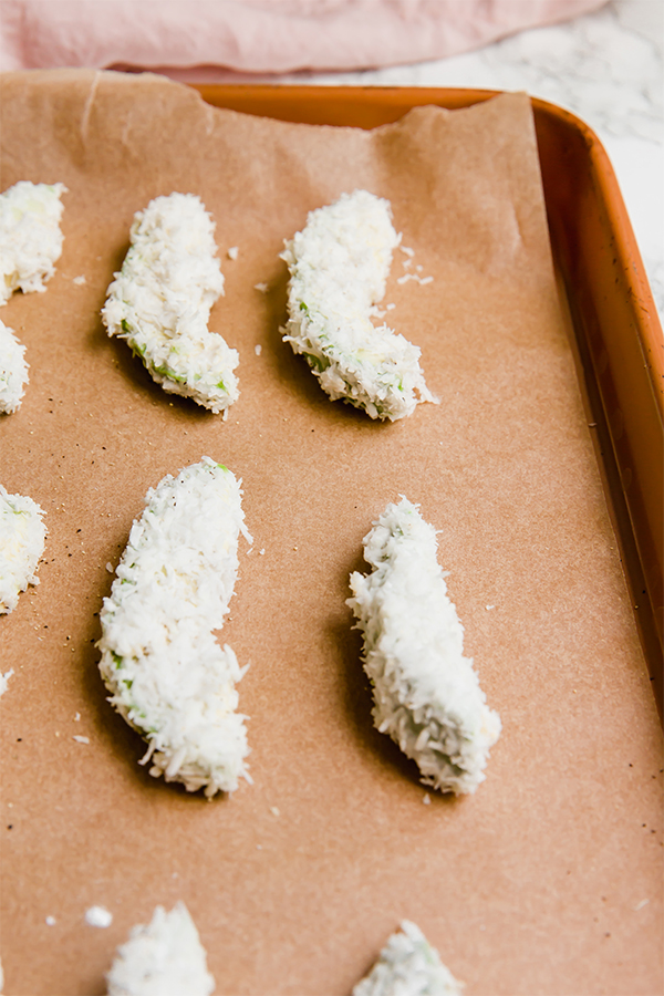 A baking sheet with parchment paper with avocado sections that have been coated before baking.