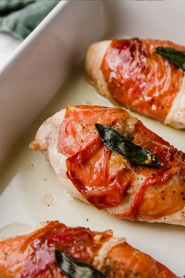 A white ceramic baking dish with pieces of proscuitto chicken after baking.