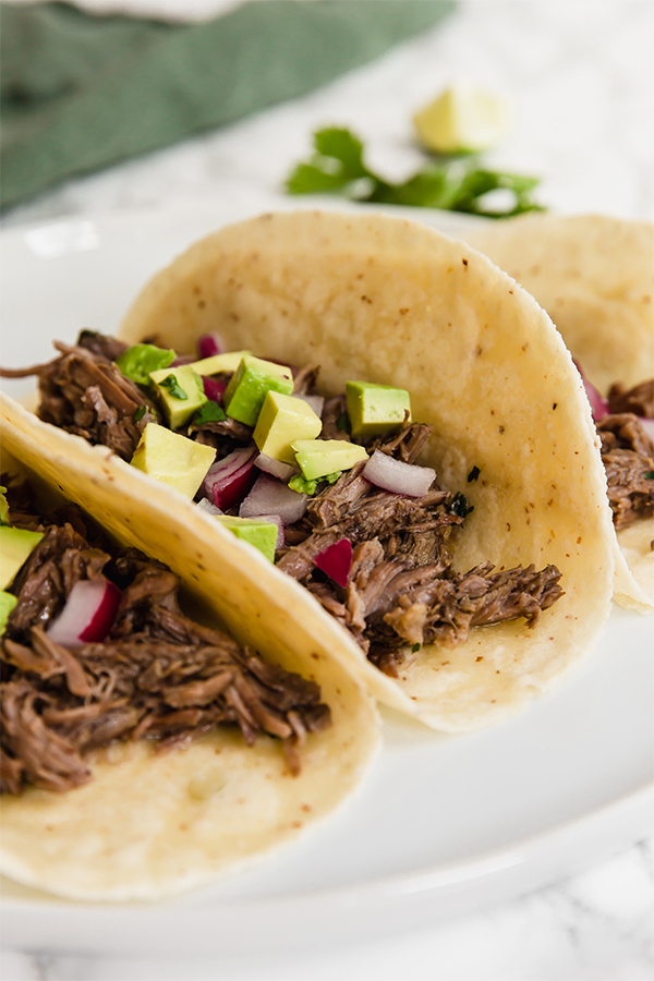 Three tacos filled with barbacoa, avocado, and onions.