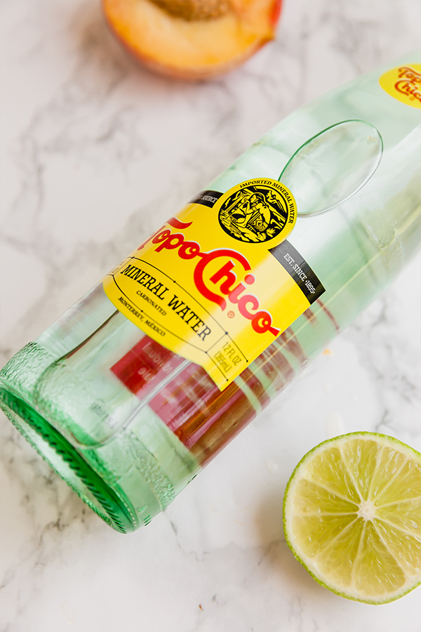 A bottle of Topo Chico lying on a counter next to a section of lime.