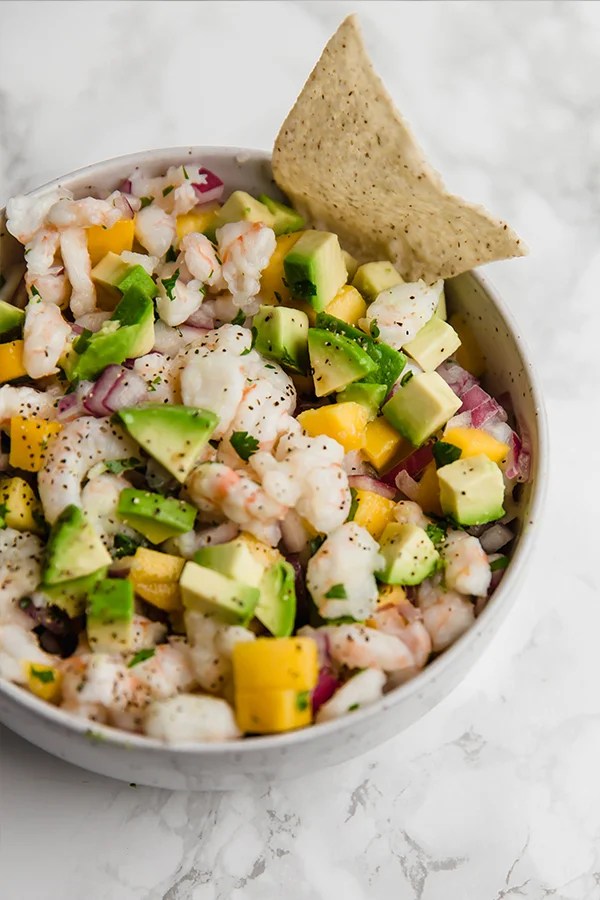 A white bowl filled with shrimp ceviche with a tortilla chip stuck in it.