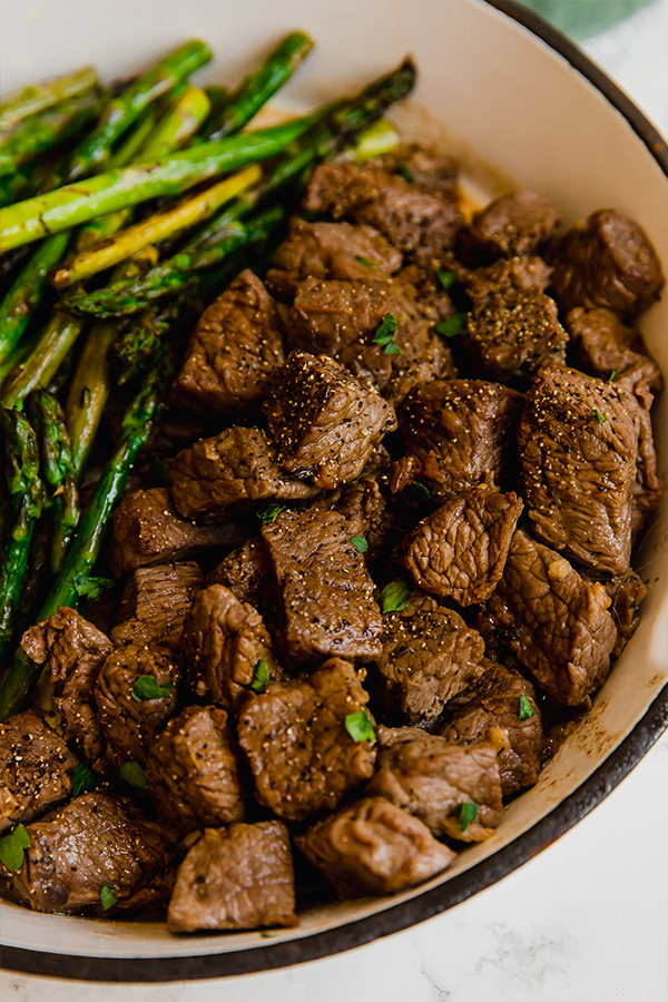 A cooking dish filled with steak bites and asparagus after cooking.