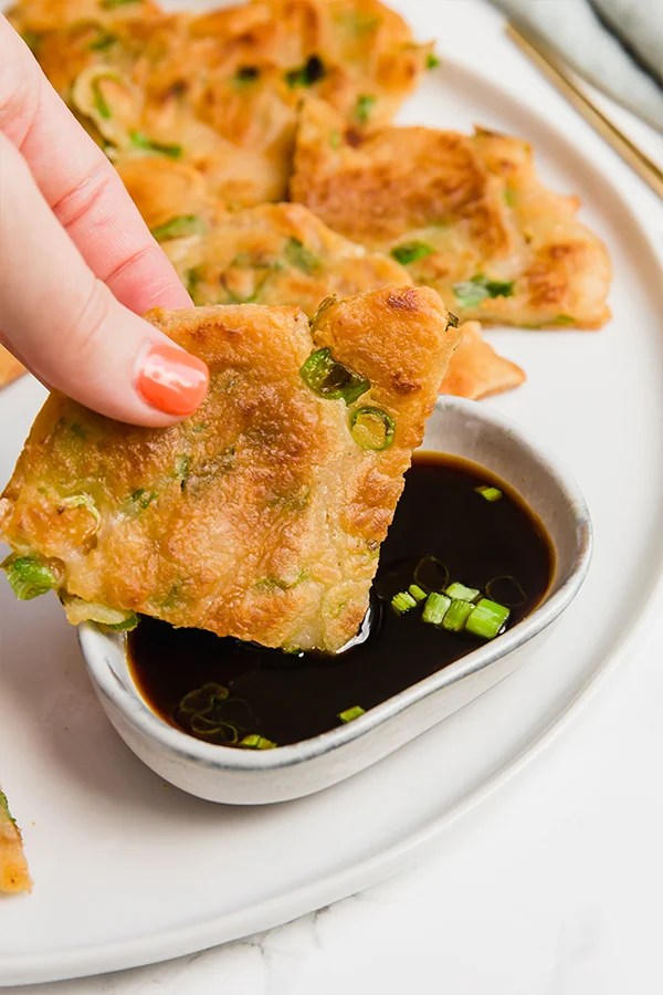 A hand dipping a quarter of a scallion pancake into dipping sauce.