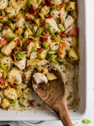 A baking dish filled with chicken bacon ranch casserole with a wooden spoon taking some out.