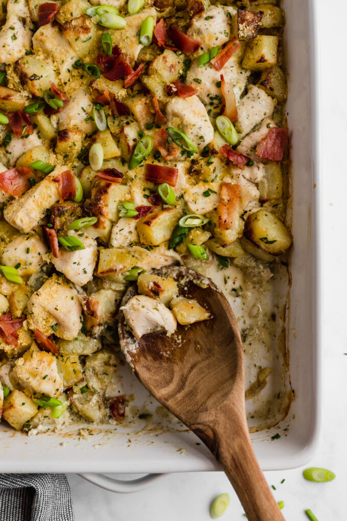 A baking dish filled with chicken bacon ranch casserole with a wooden spoon taking some out.