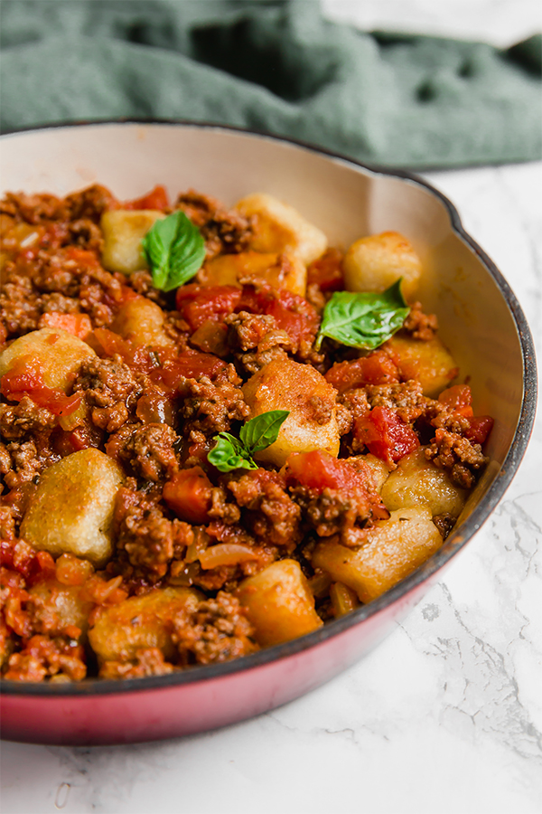 A serving dish filled with gnocchi bolognese and topped with fresh herbs.