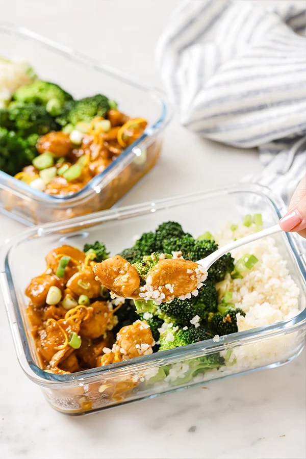 Person holding a fork full of orange chicken.