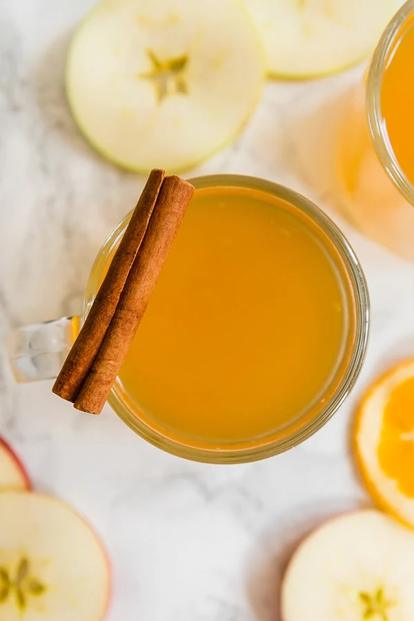 A glass filled with apple cider with a cinnamons stick resting on the side of it.