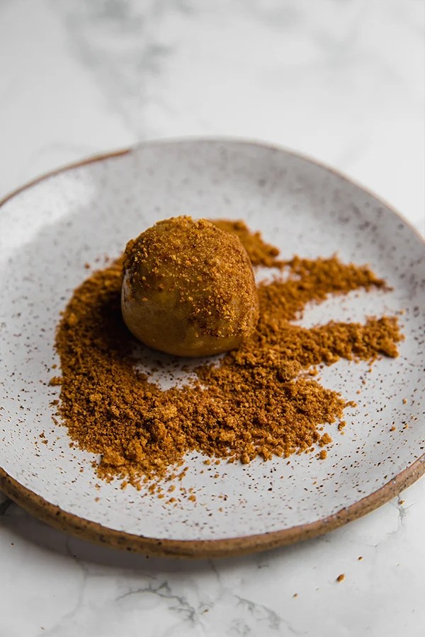 A ball of snickerdoodle dough covered in cinnamon sugar on a plate.