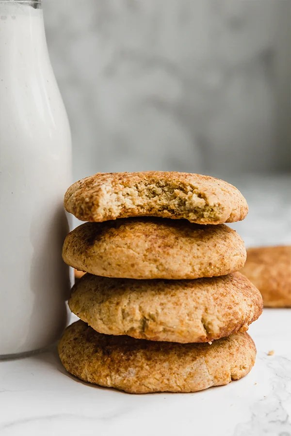 A stack of pumpkin snickerdoodle cookie next to a glass of nut milk.