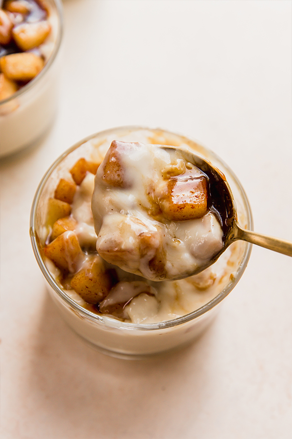 A cup of caramel vanilla pudding with a spoon in it.