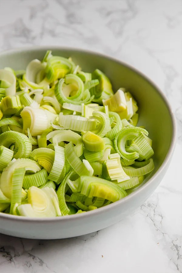 A ceramic bowl filled with prepped leeks to make carrot leek soup.