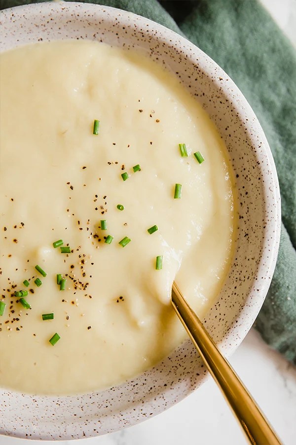 A white bowl filled with sweet potato leek soup and a soup coming out of it.