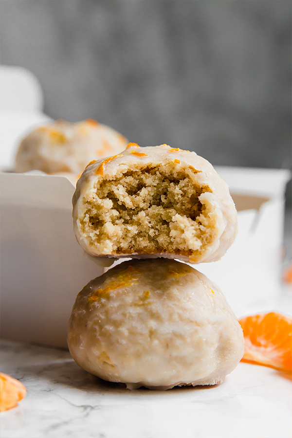Two mandarin donut holes stacked on top of each other with a bite taken out of the top one.