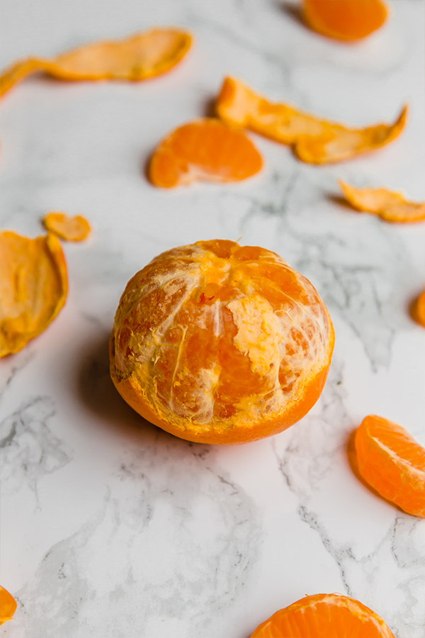 A mandarin that has been partially peeled sitting on a counter.