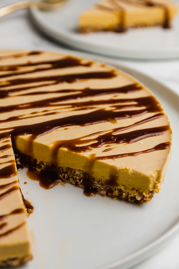 A pumpkin cheesecake on a white plate with one slice cut out.