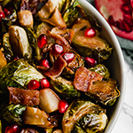 A white bowl with roasted brussels sprouts, apples, and bacon in it.