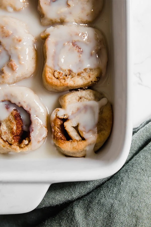 A white baking dish with AIP cinnamon rolls fully baked and covered in glaze.