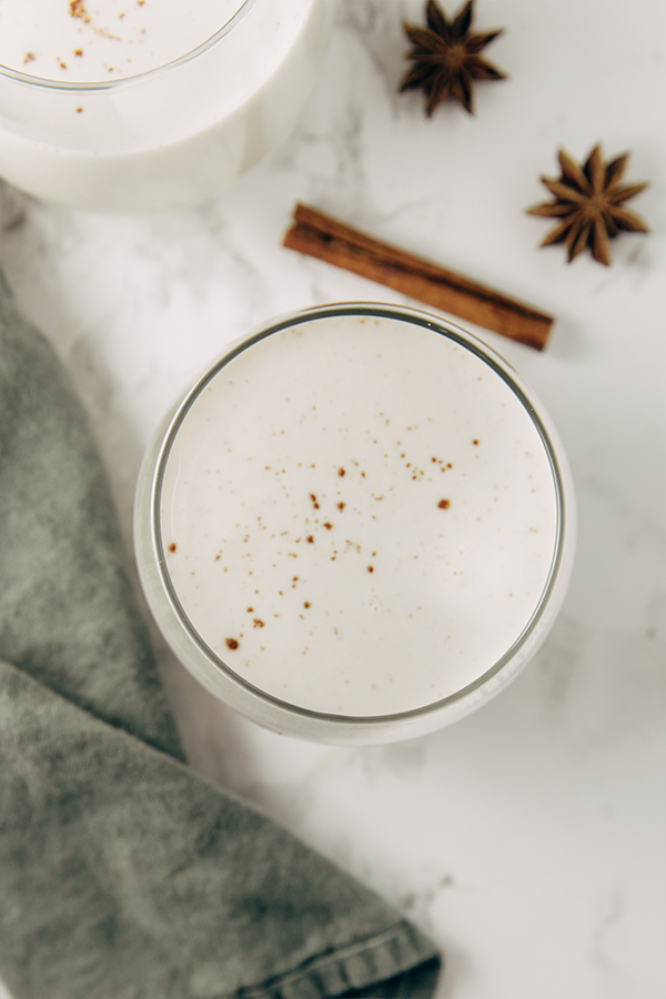 A glass of egg nog with a cinnamon stick nearby.