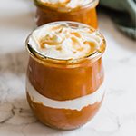 A glass container of pumpkin pie parfait in it with another jar of it behind it.
