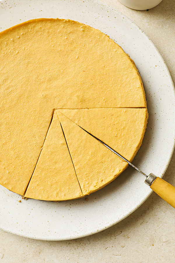 Cheesecake on a plate being cut into slices with a knife.