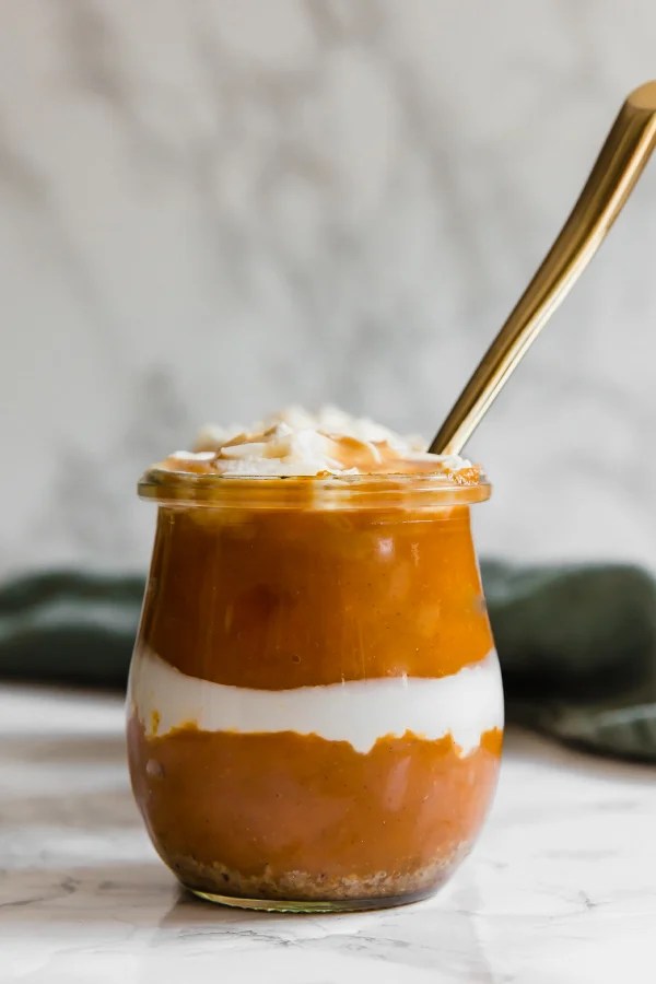 A glass container of pumpkin pie parfait in it with a spoon sticking out of it.