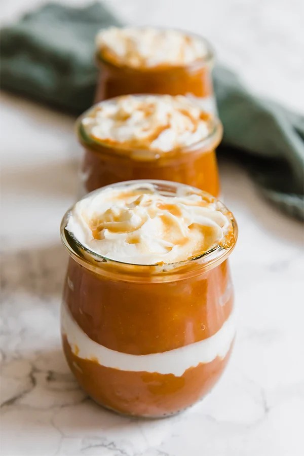 A glass container of pumpkin pie parfait in it with another jar of it behind it.