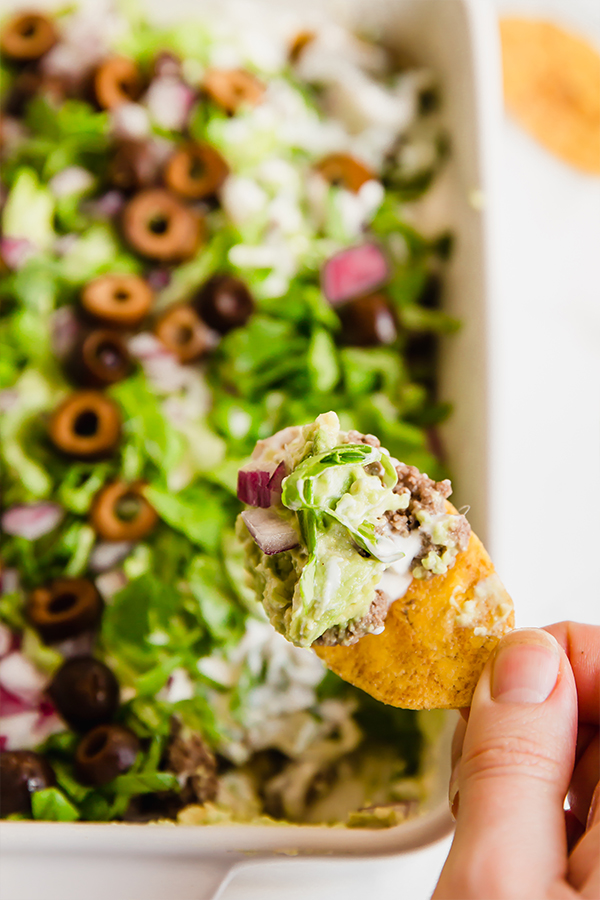 A plantain chip taking a scoop of taco dip out of a dish of taco dip.