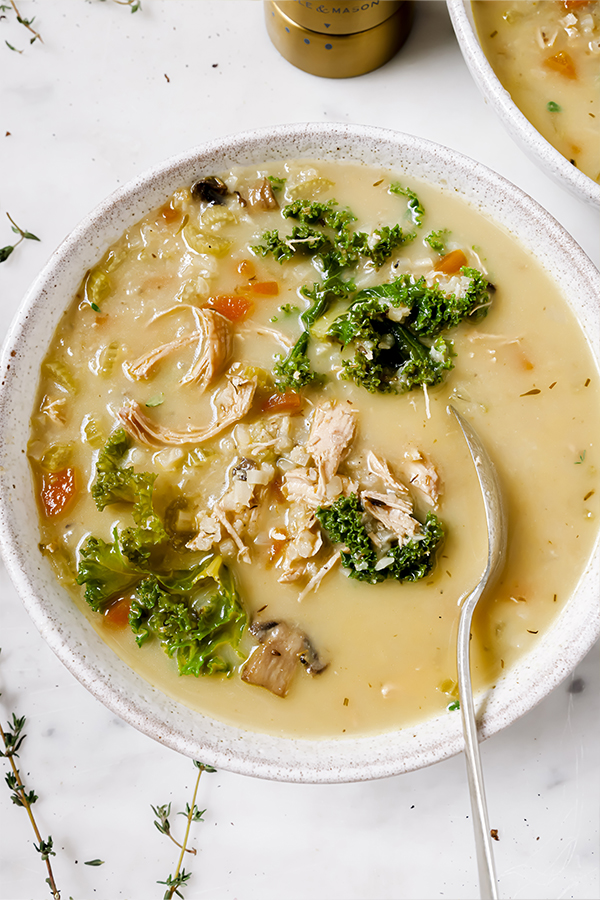 A white ceramic bowl filled with creamy turkey and vegetable soup with a silver spoon in it.