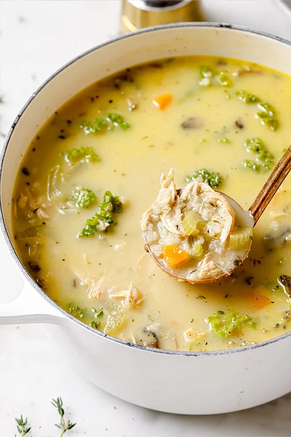 A white Dutch open filled with creamy turkey and vegetable soup with a serving spoon lifting a scoop of it out.