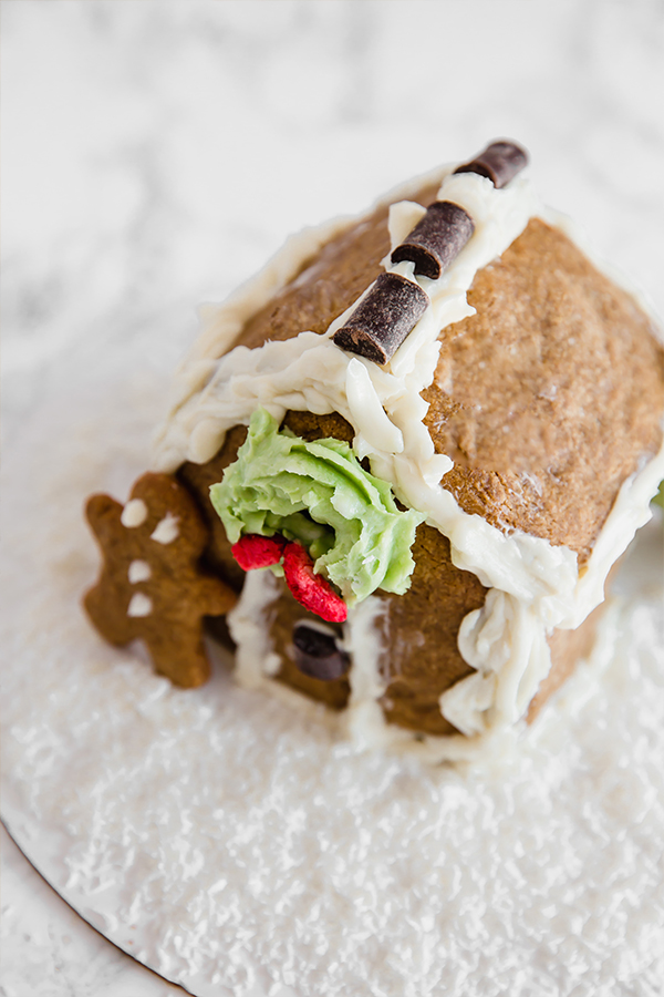 A homemade gingerbread house with a gingerbread man leaning against it.