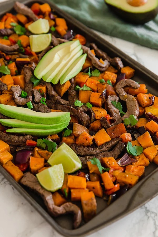 A sheet pan with breakfast taco hash on it topped with fresh sliced avocado.