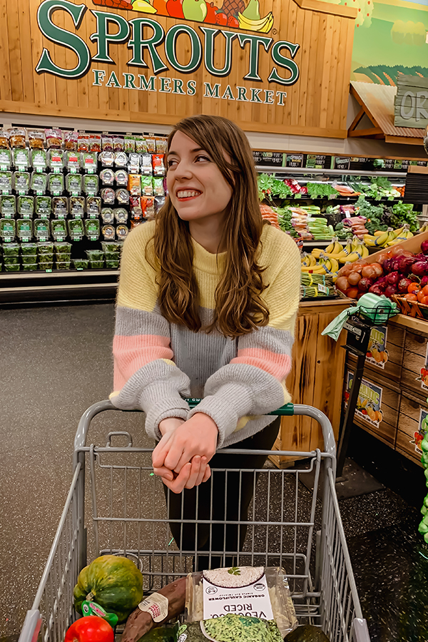 Michelle at Sprouts leaning on a shopping cart in the produce section.