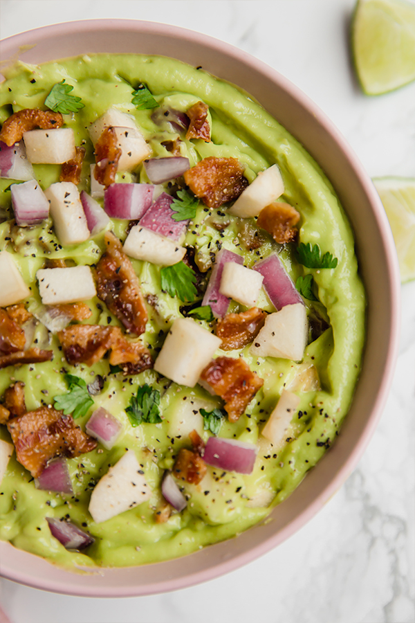 A pink bowl filled with apple bacon guacamole.