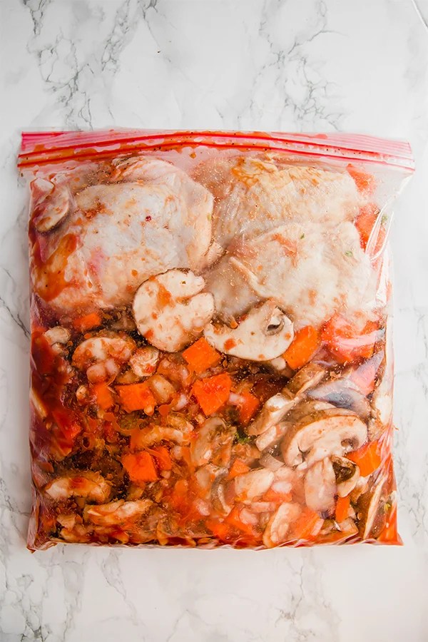 A clear plastic bowl filled with chicken cacciatore ready to be frozen.