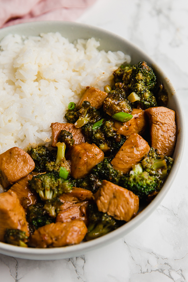 A bowl half filled with cauliflower rice and half filled with chicken and broccoli stir fry.