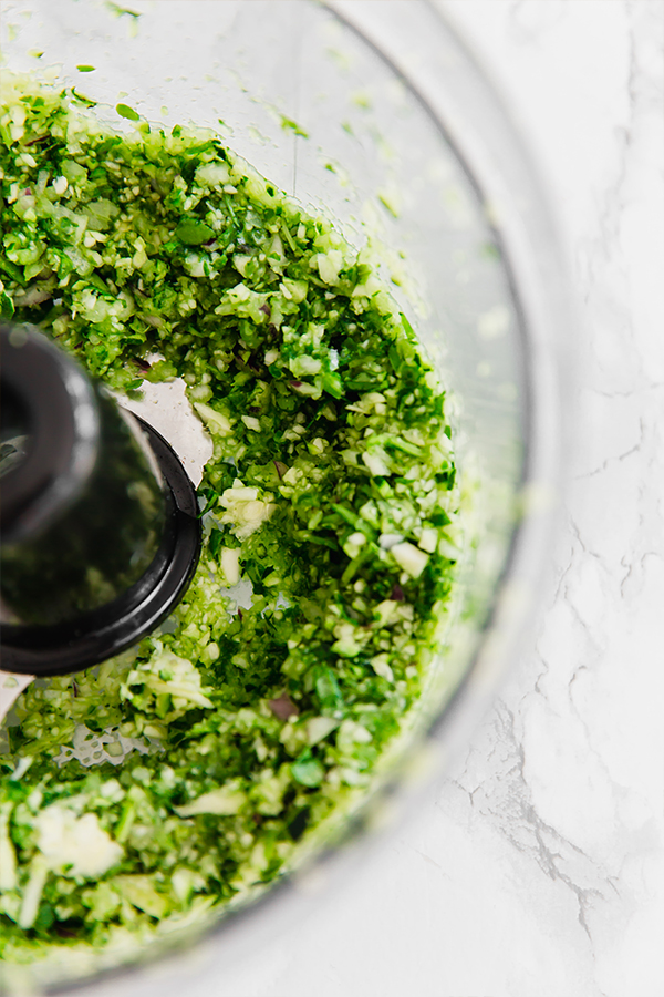 A food processor blending herbs for loaded veggie & chicken meatballs.