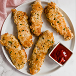 A white plate topped with homemade chicken tenders with a small container of dipping sauce nearby.