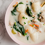 A pink bowl filled with gnocchi chicken soup.