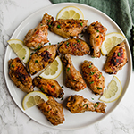 A white plate filled with lemon pepper chicken wings and slices of lemon.