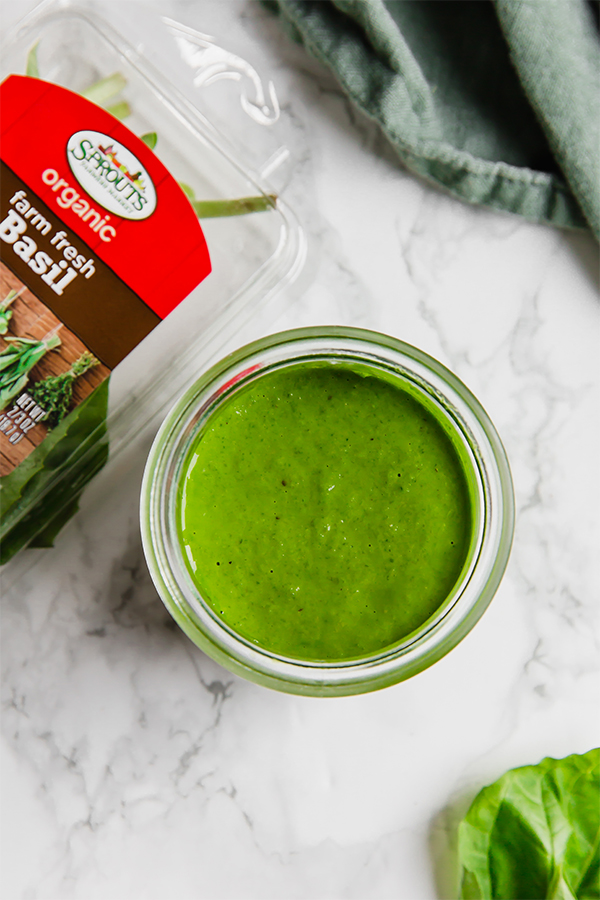 A glass jar filled with pesto sauce next to a container of fresh basil.