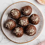 Chocolate covered samoa truffles on a small plate topped off with lightly toasted coconut.