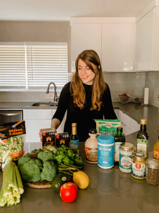 Michelle standing behind many grocery items on a counter before putting