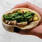 A hand holding a sausage breakfast burrito ready to be eaten.