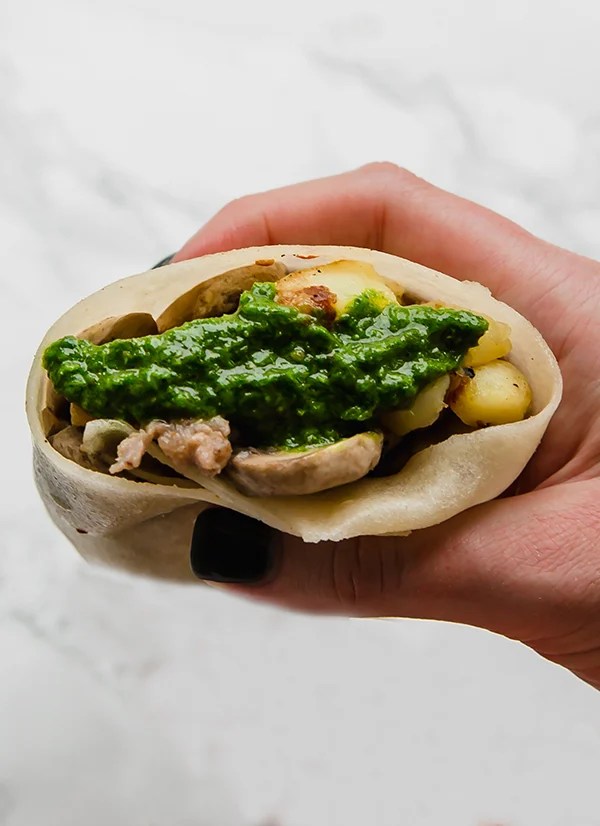 A hand holding a sausage breakfast burrito ready to be eaten.