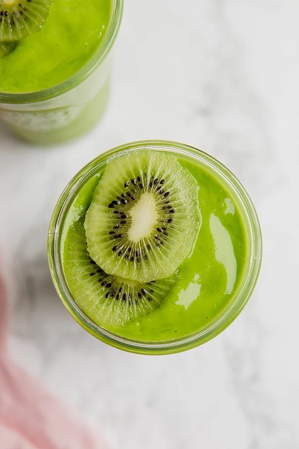 A glass filled with matcha smoothie topped with slices of fresh kiwi.