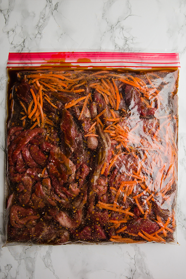 A clear plastic bowl filled with mongolian beef ready to be frozen.