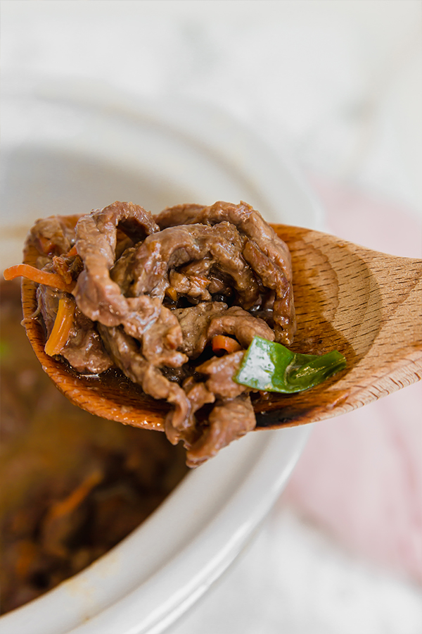 A wooden serving spoon taking a serving of Mongolian beef out.