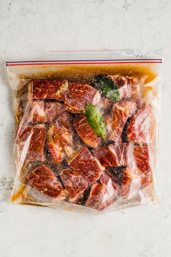 Raw beef chuck roast cut up and in a large bag with broth and bay leaves.