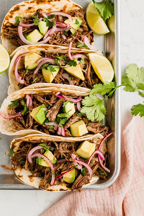 Shredded beef tacos topped with red onion, lime nad cilantro leaves.